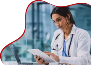 A doctor in a white coat and stethoscope uses a tablet while sitting at a desk with a laptop. The background shows a blurred office environment, and the image has a wavy red border on the left side.